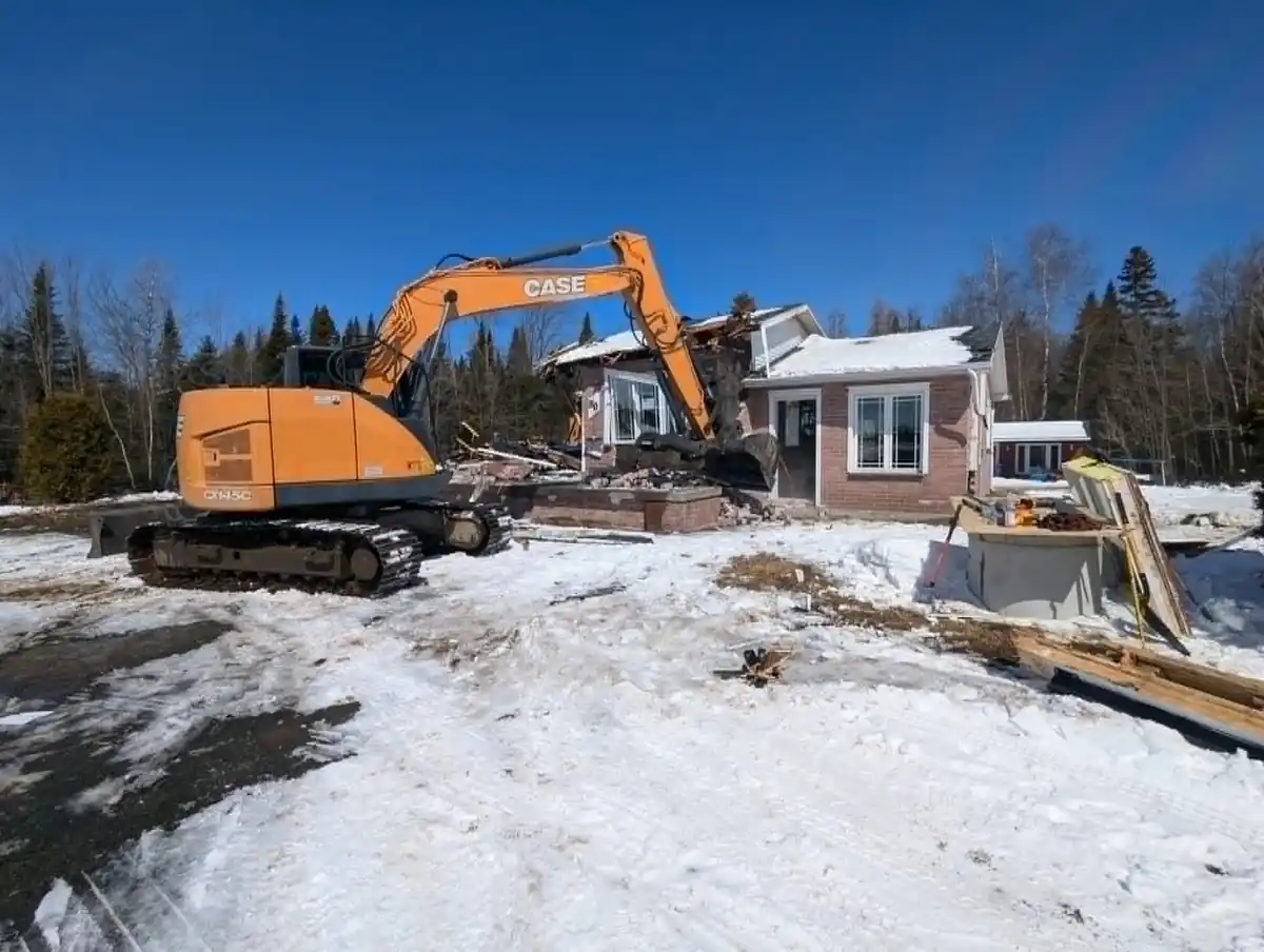 Excavatrice en train de démolir une maison résidentielle en hiver