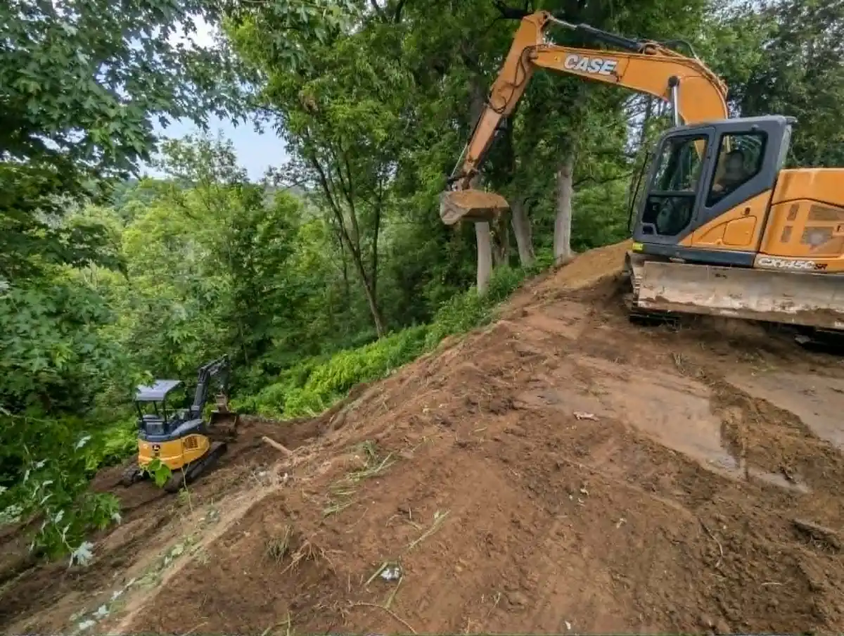 Travaux d’excavation en pente sur un terrain boisé avec deux excavatrices