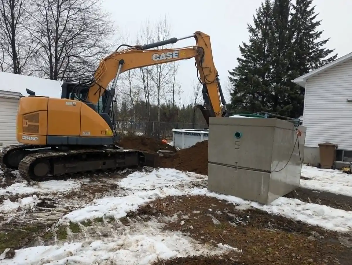 Excavatrice installant un réservoir septique sur un terrain enneigé